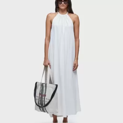 Mulher com vestido branco comprido segurar mala de tecido e óculos de sol