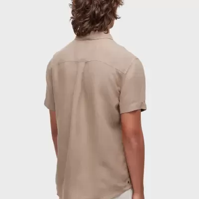 Homem de costas vestindo camisa bege de manga curta e calções brancos