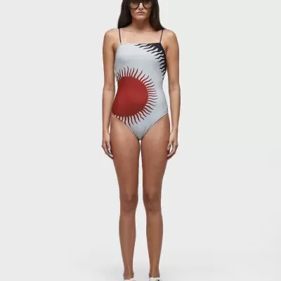 Fato de banho feminino branco com padrão circular vermelho e preto, usado com ténis brancos e óculos escuros.