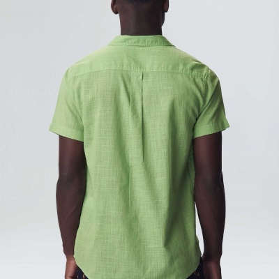 Homem de costas com camisa verde clara de manga curta e calças escuras com flores laranjas