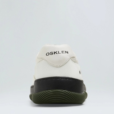 Ténis branco com sola preta e verde escura vistos pela parte traseira, com o texto OSKLEN no calcanhar