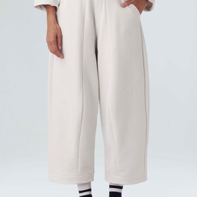 Calças largas claras com pregas frontais e cintura elástica, usadas com meias e sapatos vermelhos e bolsa pequena vermelha com etiqueta branca