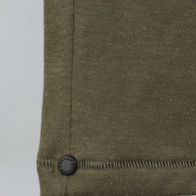 Canto inferior de tecido verde-oliva com botão preto 'MILLS' e fundo cinzento claro