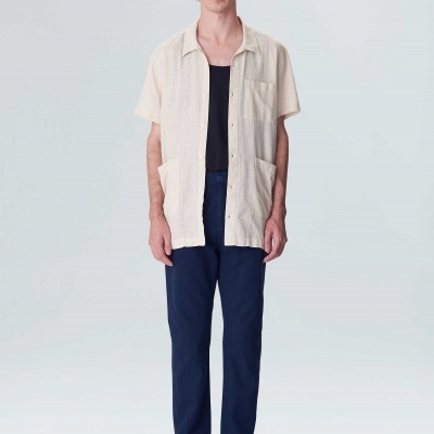 Homem com camisa bege de manga curta, calças azuis escuras e sapatos pretos