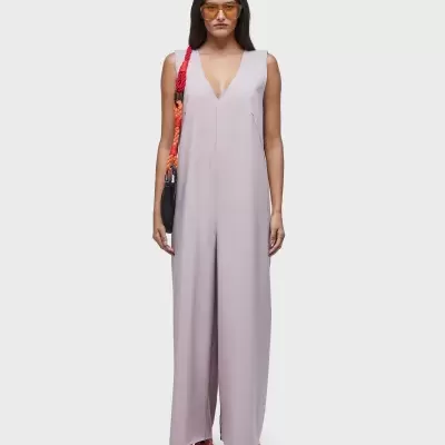 Mulher com macacão lavanda, ténis brancos e bolsa preta com alça vermelha.