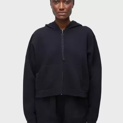 Casaco preto felpudo com capuz e fecho central usado por mulher em fundo branco