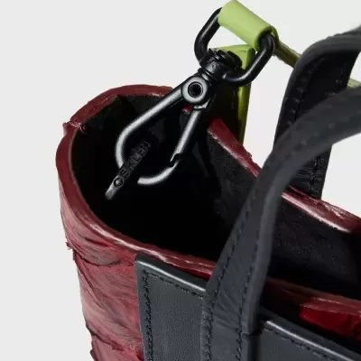 Saco em pele vermelha e preta com fecho preto e detalhe verde claro