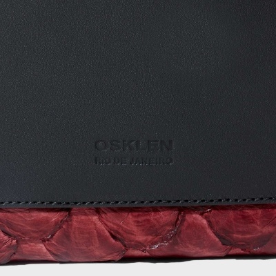 Close-up de carteira ou bolsa com textura preta lisa e vermelha escamada, com texto Osklen Rio de Janeiro