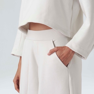 Calças e blusa creme de tecido malha com bolso e cós largo, com mão pousada no bolso