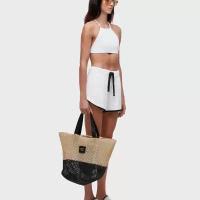 Mulher com top branco, calções brancos, óculos amarelos, sapatilhas brancas e bolsa tricotada bege e preta