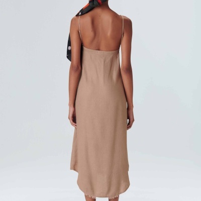 Mulher de costas a usar vestido comprido bege de alças finas, lenço vermelho e preto na cabeça e sandálias brancas