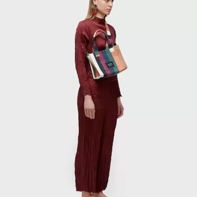 Mala de mão xadrez colorido com alças castanhas e mulher em macacão vermelho texturizado e sapatos planos bege