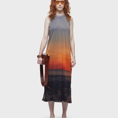 Vestido longo com padrão de pôr do sol e acessórios castanhos usado por mulher com cabelo ruivo