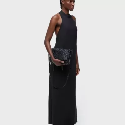 Mulher vestindo vestido preto longo e segurando mala preta com textura acolchoada