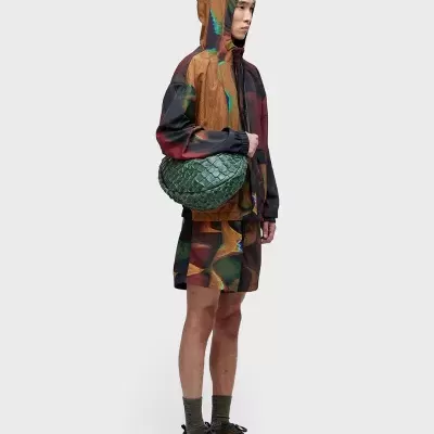 Homem com casaco e calções coloridos e bolsa verde trançada