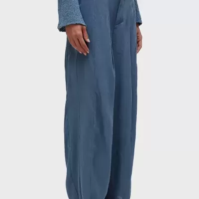 Calças largas azuis em tecido leve com cintura alta e bainha desfiada, usadas com sandálias de salto médio