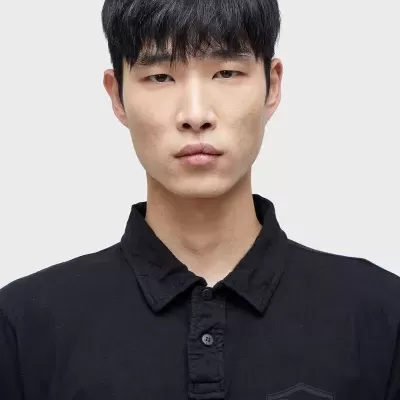 Modelo a usar uma camisola preta com gola e escudo em relevo no peito