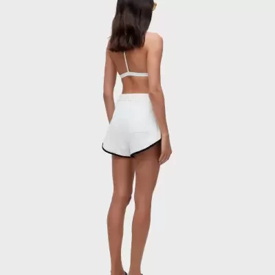 Mulher vista de costas com top branco, calções brancos com bainha preta e chinelos brancos