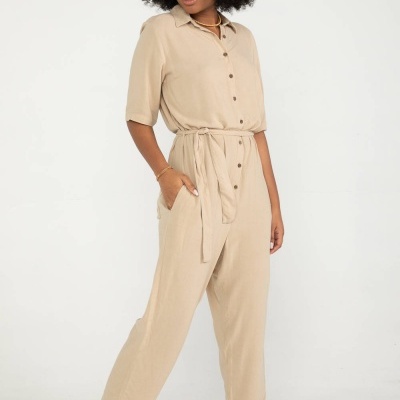 Mulher com macacão bege e sandálias bege em fundo branco