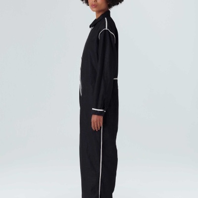 Homem com macacão preto com linhas brancas e sapatos desportivos claros em fundo branco