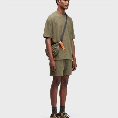Homem com roupa verde cáqui e mochila pequena acolchoada com etiqueta laranja