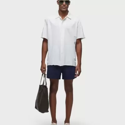 Homem com camisa branca, calções azuis, ténis brancos e mala preta