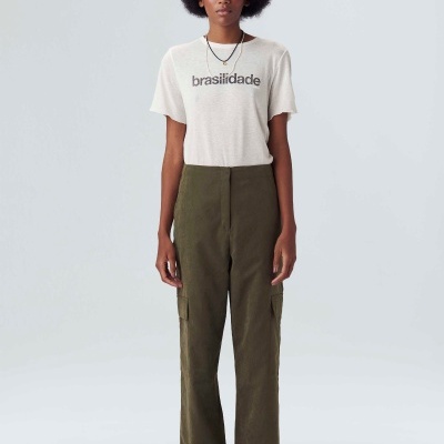 Mulher com t-shirt branca com texto preto e calças cargo verdes em fundo branco.