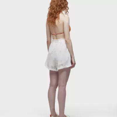 Mulher vista de costas com top laranja, saia branca transparente e ténis brancos