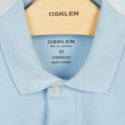 Polo azul claro OSKLEN M com colarinho e botões num cabide de madeira OSKLEN