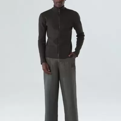 Homem com camisola preta de fecho, calças largas cinza e ténis bege