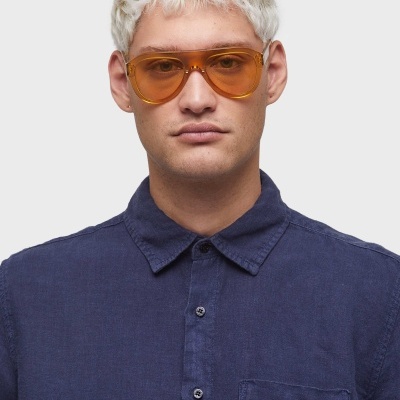 Homem a usar óculos de sol com armação castanha translúcida e camisa azul escura