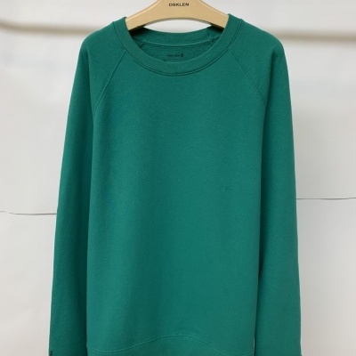 Camisola verde de manga comprida com gola redonda pendurada num cabide de madeira.