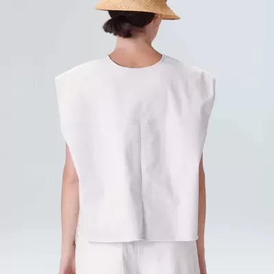 Pessoa de costas com chapéu de palha bege e roupa branca, fundo cinza claro