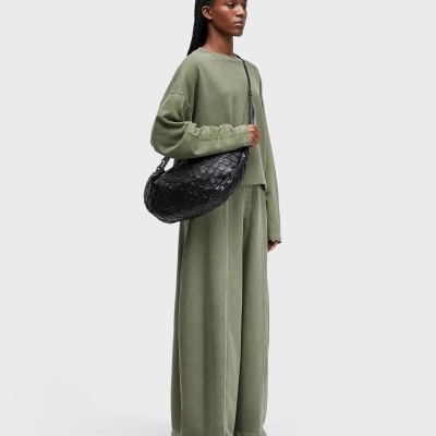 Mulher com conjunto verde e mala preta texturada em fundo branco