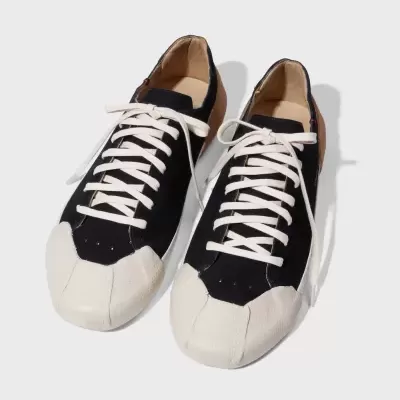 Ténis pretos com biqueira e atacadores brancos sobre fundo branco