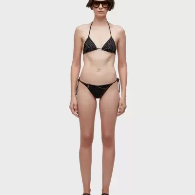 Modelo com biquíni preto com padrão geométrico cinza, sapatilhas pretas e óculos escuros.