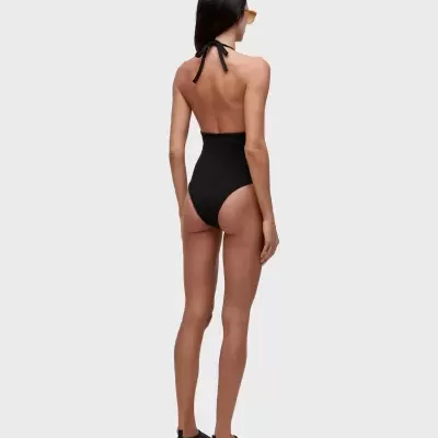 Modelo vista de costas com fato de banho preto, óculos de sol amarelos e sapatilhas pretas