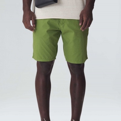 Homem com calções verdes, ténis brancos e bolsa preta com fundo cinza