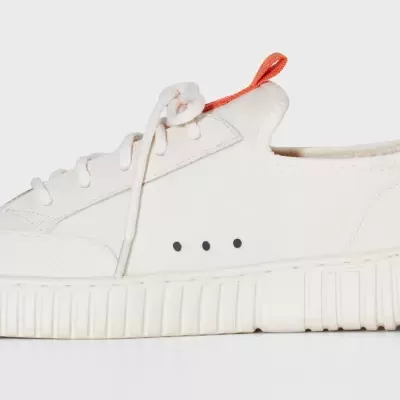 Ténis branco com sola grossa e riscada, atacadores brancos e alça laranja