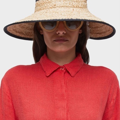 Mulher com blusa coral, chapéu de palha com lenço estampado e óculos de sol amarelos