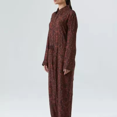 Macacão comprido com padrão floral vermelho e preto, usado por uma mulher com sandálias.