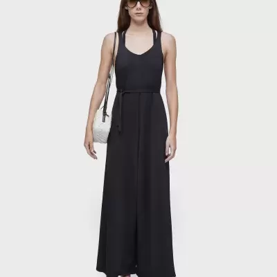 Mulher com vestido preto comprido, sandálias e mala branca