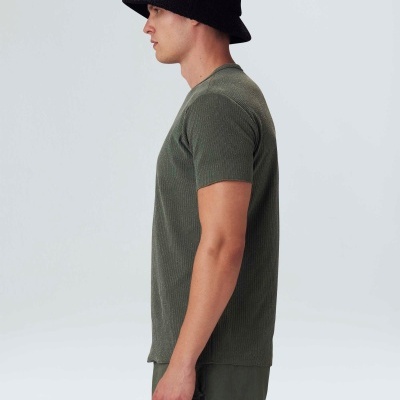 Homem de perfil com chapéu preto, t-shirt verde canelada e calças verdes