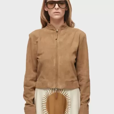 Mulher a usar blusão castanho com fecho, saia branca com padrão castanho e óculos de sol.