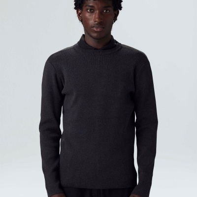 Homem com camisola preta de malha e calças pretas em fundo branco