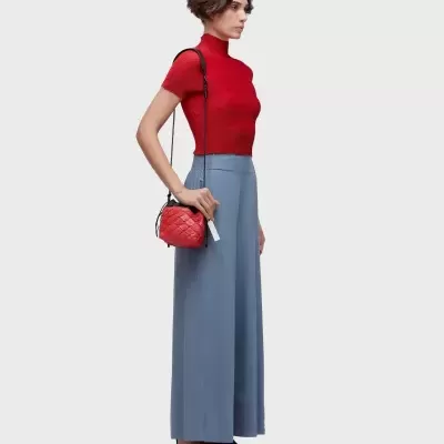 Mulher com blusa vermelha de malha, calças largas azul claro, sapatilhas pretas e bolsa vermelha pequena.