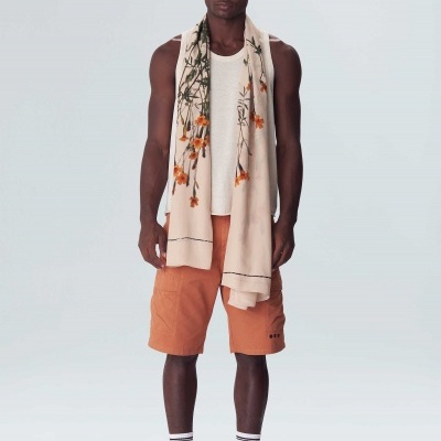 Homem com camisola branca de alças, calções laranja, cachecol floral bege e sapatilhas claras