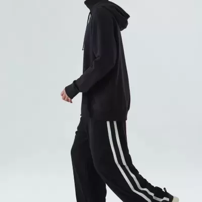 Modelo masculino com conjunto desportivo preto com riscas brancas em fundo branco