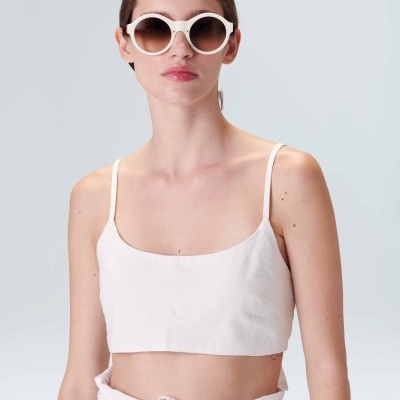 Mulher com óculos de sol redondos brancos e roupa branca em fundo cinza claro