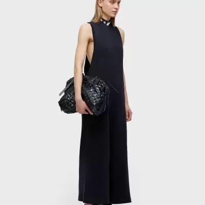 Macacão preto feminino com gola alta, bolsa preta grande e sapatos pretos